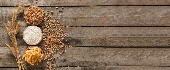 Raw pasta, wheat flour and grains on wooden background with space for text