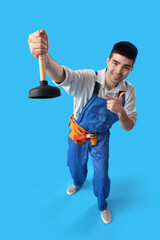 Young male plumber pointing at plunger on blue background