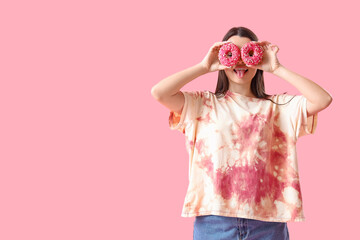 Funny young woman in tie-dye t-shirt and with donuts on pink background