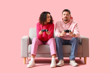 Upset young couple playing video game on pink background