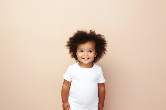 design mockup: cute black baby girl wearing white blank shirt or bodysuit on a pastel brown background, studio shot