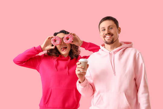Young couple with tasty donuts and cup of coffee on pink background
