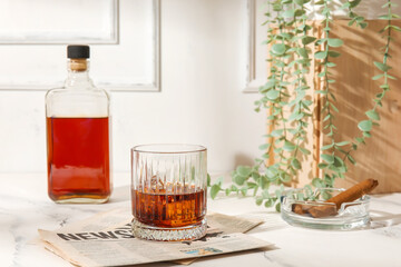 Glass of cold rum, newspaper and ash tray with cigar on table