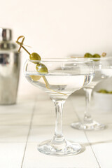 Glasses of tasty martini and olives on white tile table