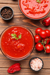 Bowls with tasty tomato sauce and fresh vegetables on wooden background, closeup