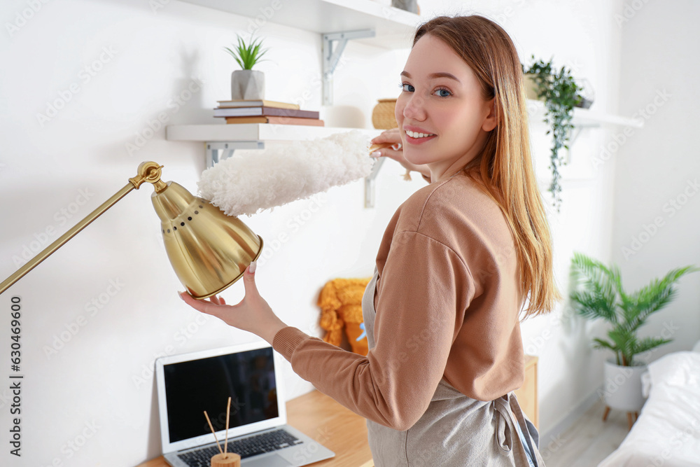 Wall mural Young woman cleaning lamp in bedroom