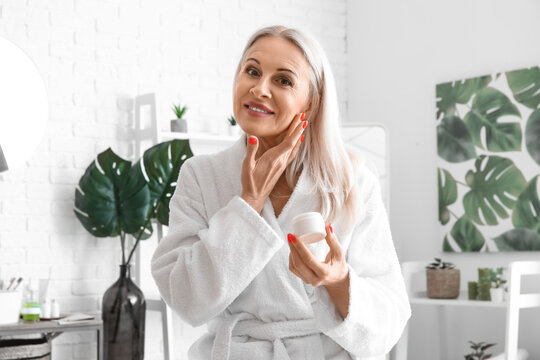 Mature woman applying facial cream in bathroom
