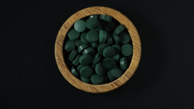 Green Spirulina pills in wooden bowl on dark background. 4K video, rotating. Pressed pills from seaweed extract are widely used in alternative medicine.