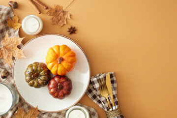 Autumn table serving concept. Top view of pumpkins on the plate, cutlery, tablecloth, candles, leaves, napkin, anise, cinnamon, acorns on pastel brown background with blank space for ads or text