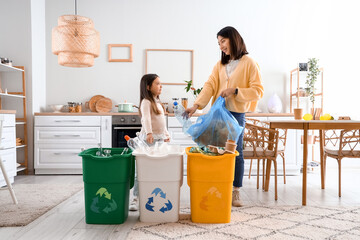 Asian mother with her little daughter sorting garbage with recycle bins in kitchen