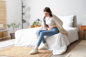 Young woman having menstrual cramps in bedroom - obrazy, fototapety, plakaty