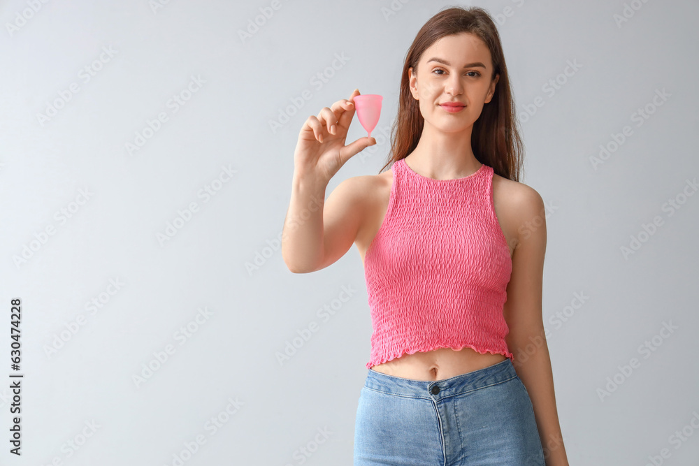 Wall mural Young woman with menstrual cup on light background