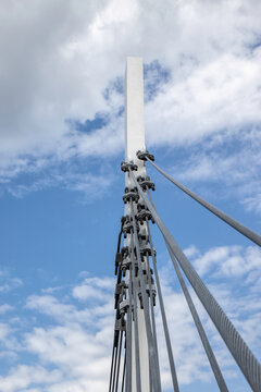 Large rectangular wooden bridge support column fastened by heavy steel braided guy wires and turnbuckles, blue sky with clouds, nobody