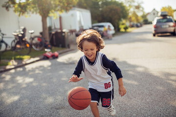 Young boy playing with a basketball on the street in the suburbs