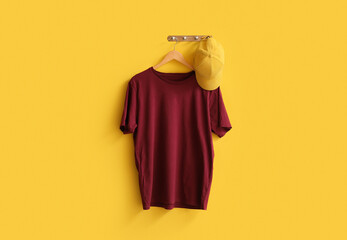 Stylish red t-shirt and cap hanging on yellow background