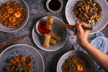 Close up of a person's hand using chopsticks with Chinese food