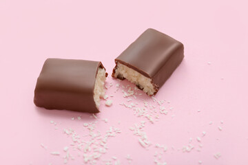 Halves of tasty chocolate covered coconut candy on pink background