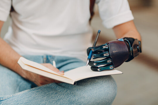 Cropped image of a person with prosthetic hand writing on a notebook