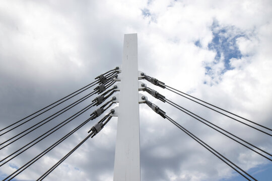 Large rectangular wooden bridge support column fastened by heavy steel braided guy wires and turnbuckles, blue sky with clouds, nobody
