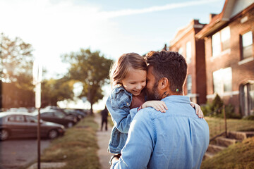 Father and daughter hugging on a sidewalk in the suburbs of a city