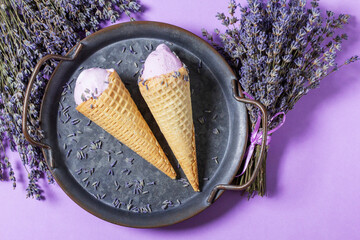 Two lavender ice creams in waffle cones on a tin tray and bouquets of dry lavender on a lilac background. - 630485296