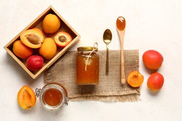 Jars and wooden spoon with sweet apricot jam on white background