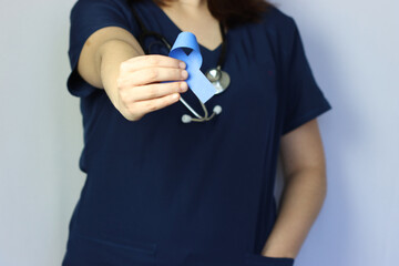 Blue ribbon in a woman’s hand. Woman wearing surgical scrubs holding the blue ribbon. 