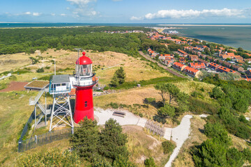 Fototapeta na wymiar Aerial drone image of the island Vlieland. With bright red lighthouse on top of a sand dune overlooking the small town, Terschelling, the North Sea and the Wadden Sea. Blue sky, summer and red roofs