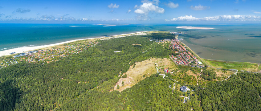 Aerial drone image of the island Vlieland. With bright red lighthouse on top of a sand dune overlooking the small town, Terschelling, the North Sea and the Wadden Sea. Blue sky, summer and red roofs