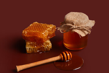 Jar of sweet honey with combs and dipper on red background
