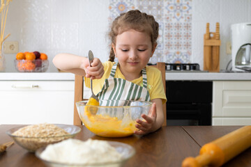 happy child helping in kitchen. kid cooking food. little cute girl in apron in preparing dough,...