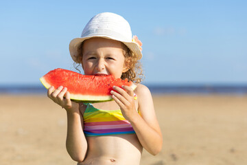 cute little girl eats ripe juicy red watermelon on the beach, coast, seashore. the concept of summer kid holidays, seasonal fruits and berries