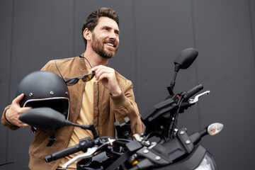 Stylish smiling confident man, biker wearing helmet standing near sport motorcycle