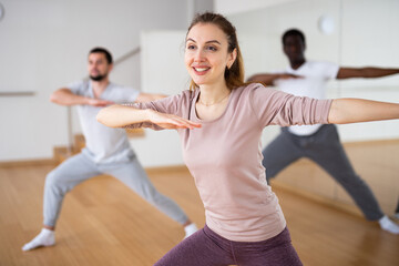 Cheerful woman dancing aerobic dance to warm up during group fitness training in studio.
