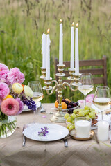 Elegant fancy wedding table decor with bright ranunculi flowers in a vase outdoors, chandelier, field or meadow. Summer, sunset, golden hour. Romantic dinner for a couple in restaurant outside