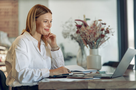 Smiling business woman working on laptop, making notes in cozy coworkign space interior