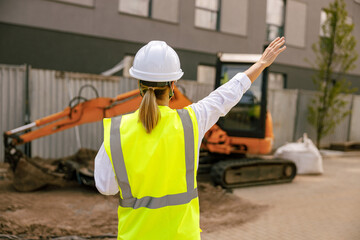 Back view of female construction worker in protective helmet against on construction background 