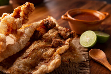 Chicharron. Crispy Fried pork rind, are pieces of aired and fried pork skin, traditional Mexican ingredient or snack served with lime juice and red hot sauce.