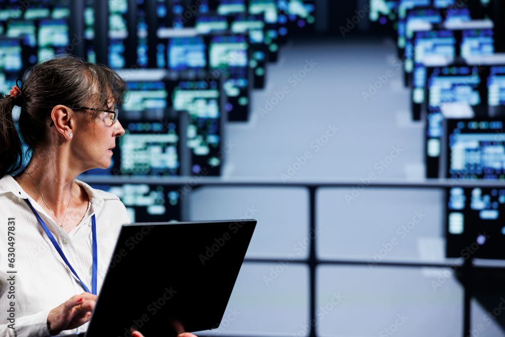 Poster experienced technician in data center working on laptop, setting up high bandwidth dedicated multipl