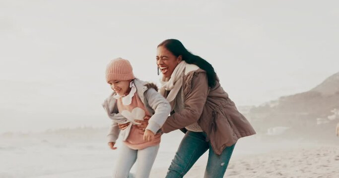 Playing, hug and a mother and child at the beach for a holiday, love or running together. Happy, playful and a young mom ahd a girl kid at the ocean in winter for bonding, care and a vacation