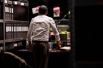 Detective analyzing crime weapon and photos attached to wall, searching insight. African american...