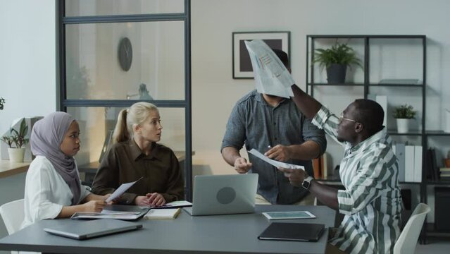 Group of multi-ethnic managers sitting at table in office refusing to listen to their colleague and offending him during meeting