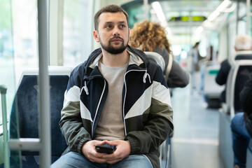 Interested young man browsing messages on phone on way to work in modern streetcar ..