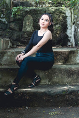 A young fashionable young asian woman in a black top and dark blue jeans sitting on damp concrete stairs.