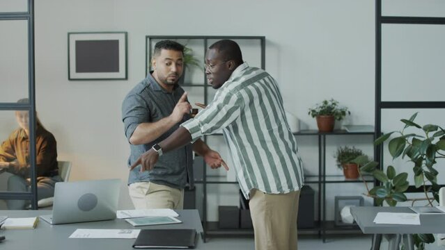 Medium long shot of African American and Middle Eastern male colleagues starting fight in office