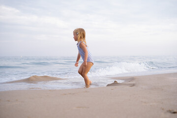 Fototapeta na wymiar Little girl with long hair running looking at sea waiting on sandy beach at Mediterranean seaside in Spain. Carefree childhood, freedom, happiness concept.