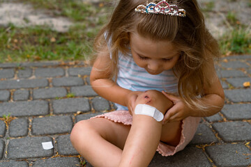 A little girl puts a band-aid on a wound on her knee after an accident. Selective focus.