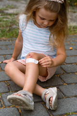 A little girl puts a band-aid on a wound on her knee after an accident. Selective focus.