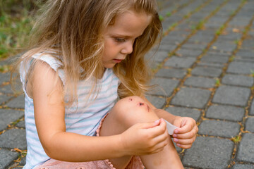 A little girl puts a band-aid on a wound on her knee after an accident. Selective focus.