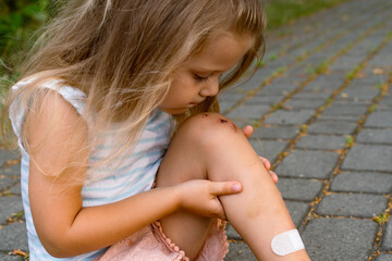 A little girl puts a band-aid on a wound on her knee after an accident. Selective focus.